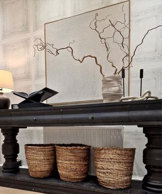 An entryway with a black console table with wicker baskets underneath it, and white walls