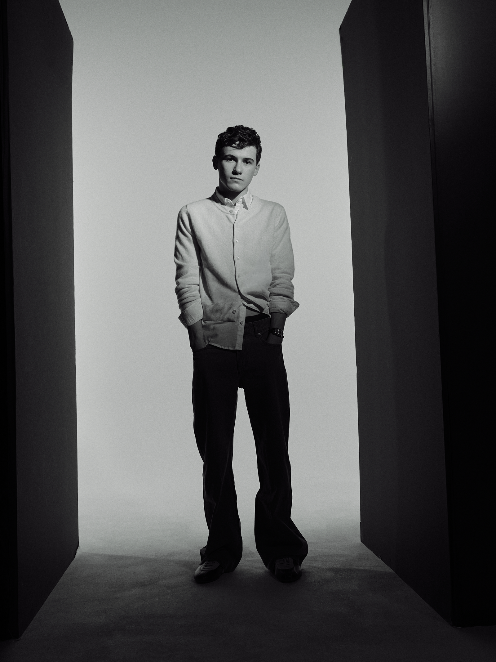Actor Sam Nivola, photographed by JJ Geiger for Who What Wear. He is wearing a white button-down shirt and khaki trousers with a yellow cardigan.