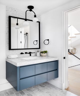 Blue vanity with drawers and square mounted mirror over black faucets