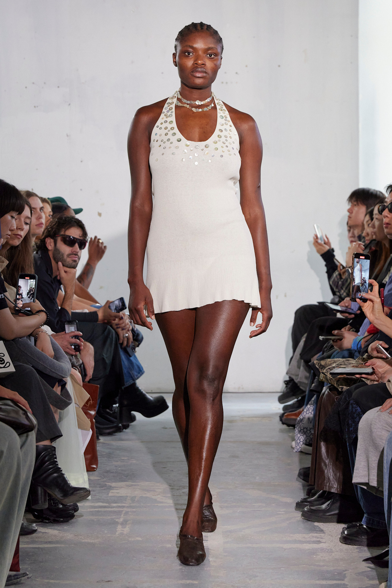 A Paloma Wool model walking down the runway in a button-embellished halterneck dress