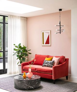 Bright pink red couch in small living room with pale pink walls, throw pillows and fiddle leaf fig