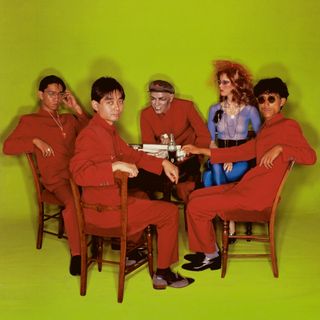 Solid State Survivor album cover. A group of men sitting on wooden chairs wearing orange overalls.