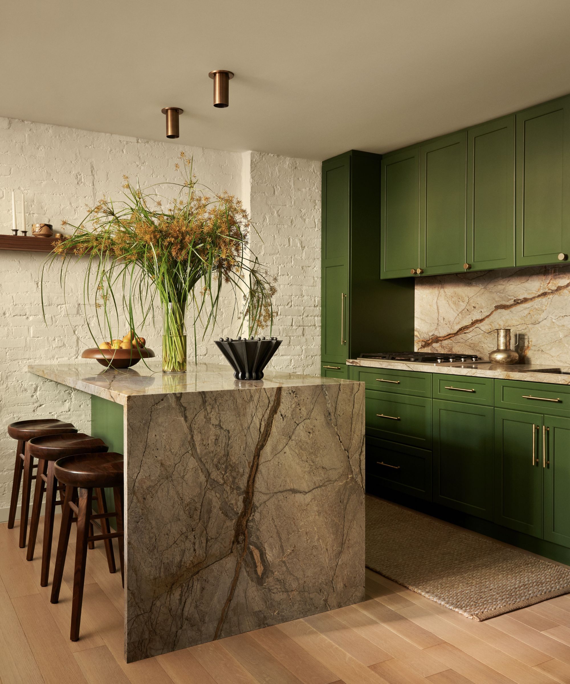 kitchen with white painted brick wall, green cabinetry, marble island