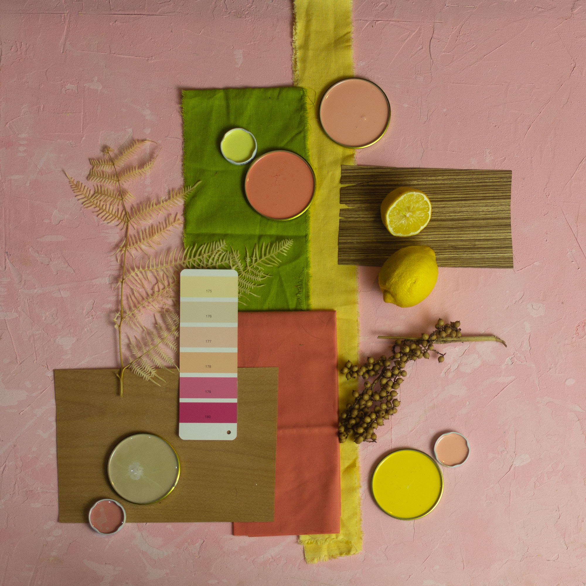 colorful moodboard on pink plaster background with green and yellow fabric and pink and yellow paints along with other accessorize
