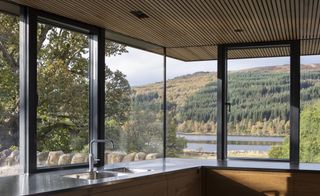 Kitchen with wood ceilings, windows all around and view of forest and lake