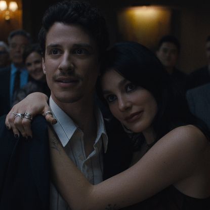 Adam DiMarco as Nicky Cunningham, Camila Morrone as Rachel Harkin in episode 105 of Something Very Bad Is Going To Happen wearing formal wear and standing arm in arm as they talk to another couple at a party