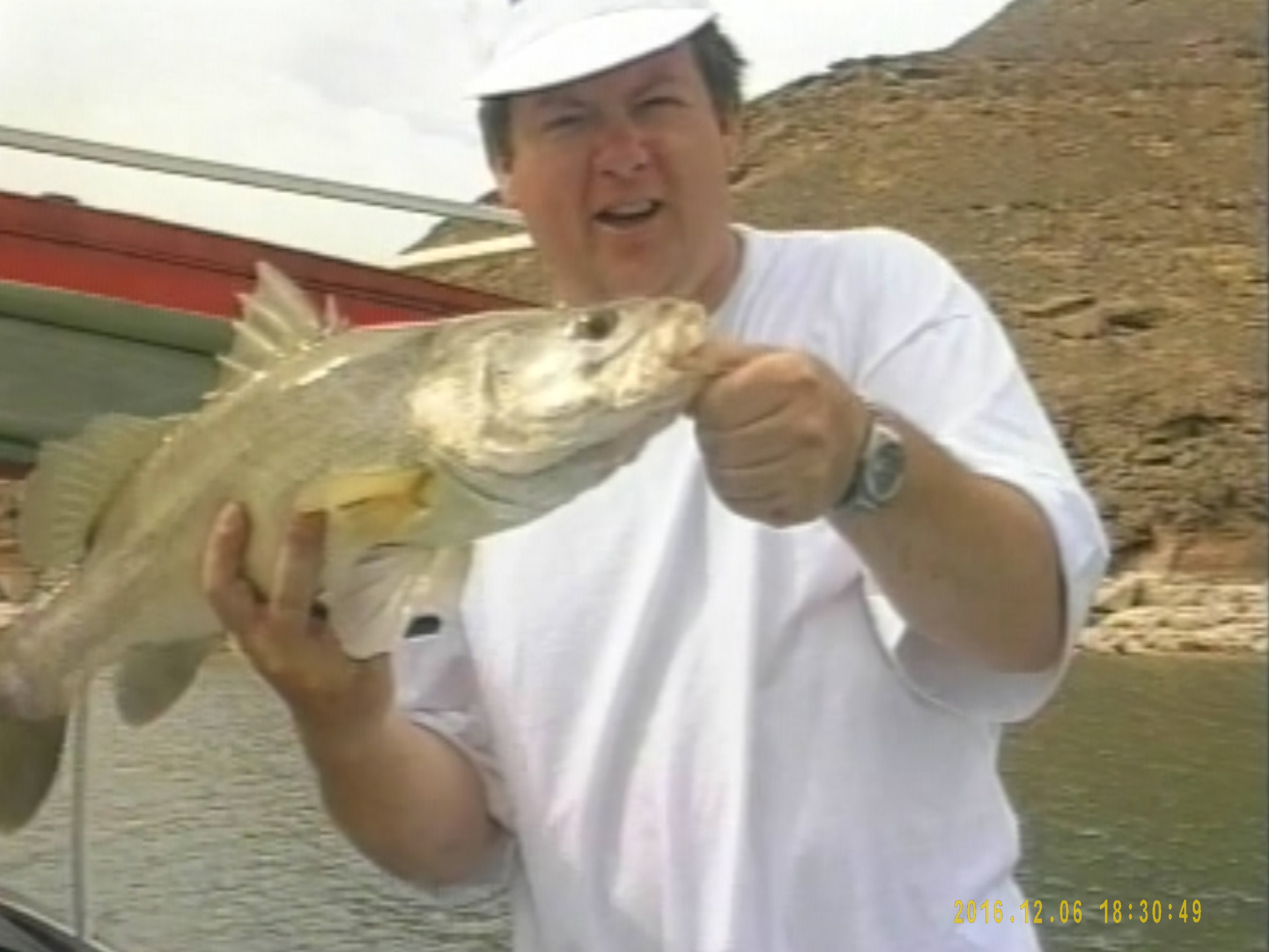 A screenshot of a man holding a large fish, taken from a fishing highlights DVD