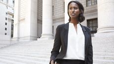 A professional woman stands on the steps of a courthouse.