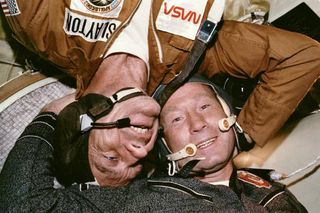 an astronaut and a cosmonaut put their heads together in space. one is floating upside down