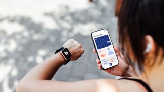 Young woman looking at fitness tracker data on smartphone and on wrist