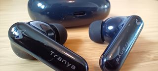 A pair of black Tranya Nova earbuds sitting on a wooden desk