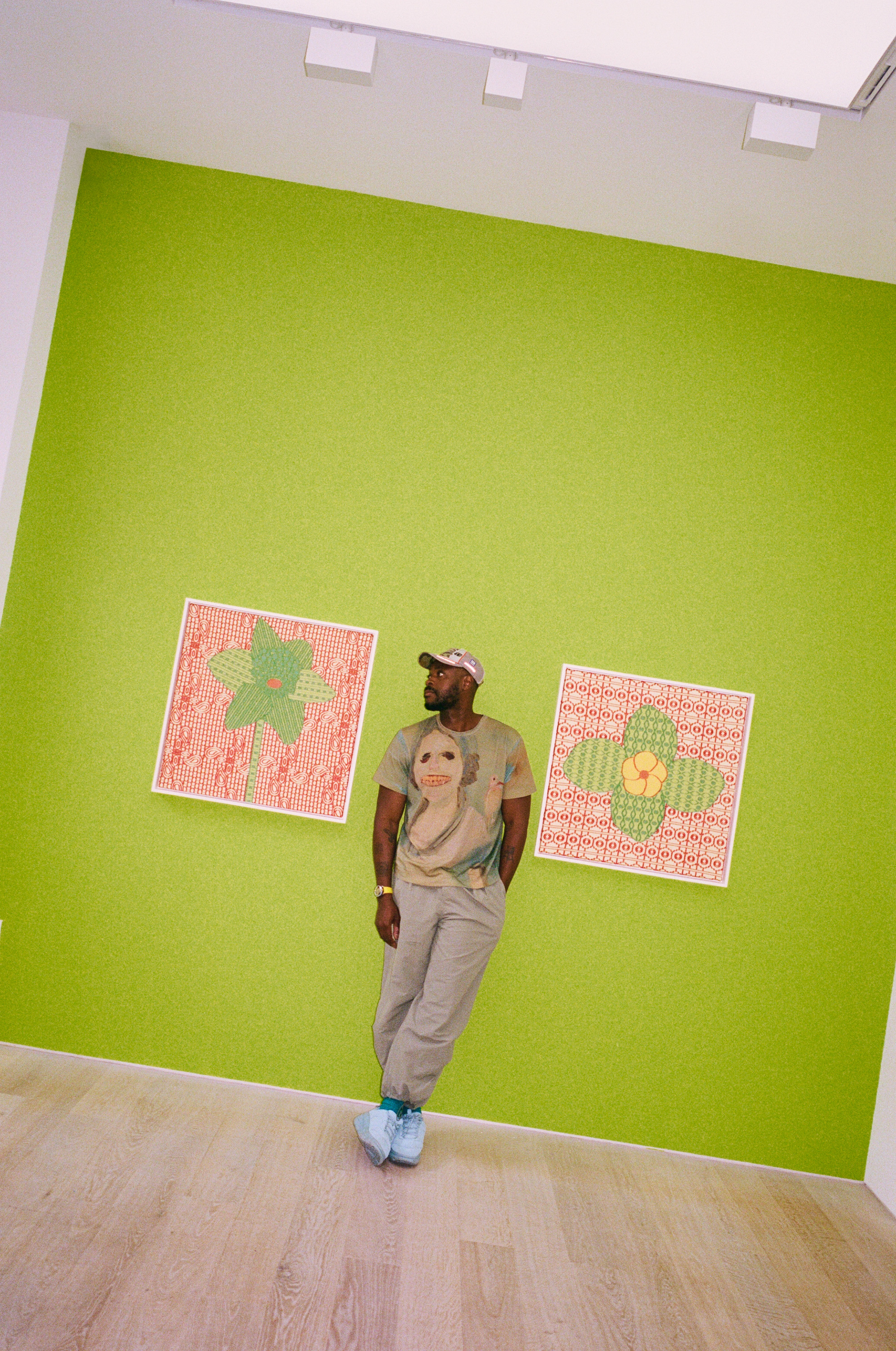 Yinka Ilori stands against a green wall between two pink and green flower prints
