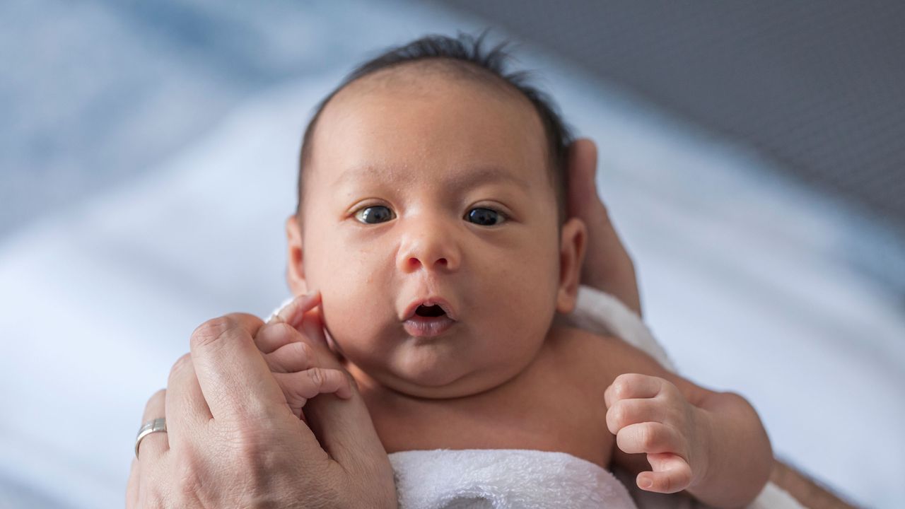 A newborn baby looks at his mother, wide-eyed.