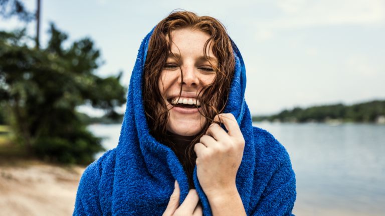 A woman standing on a beach while wrapped in one of the best travel towels