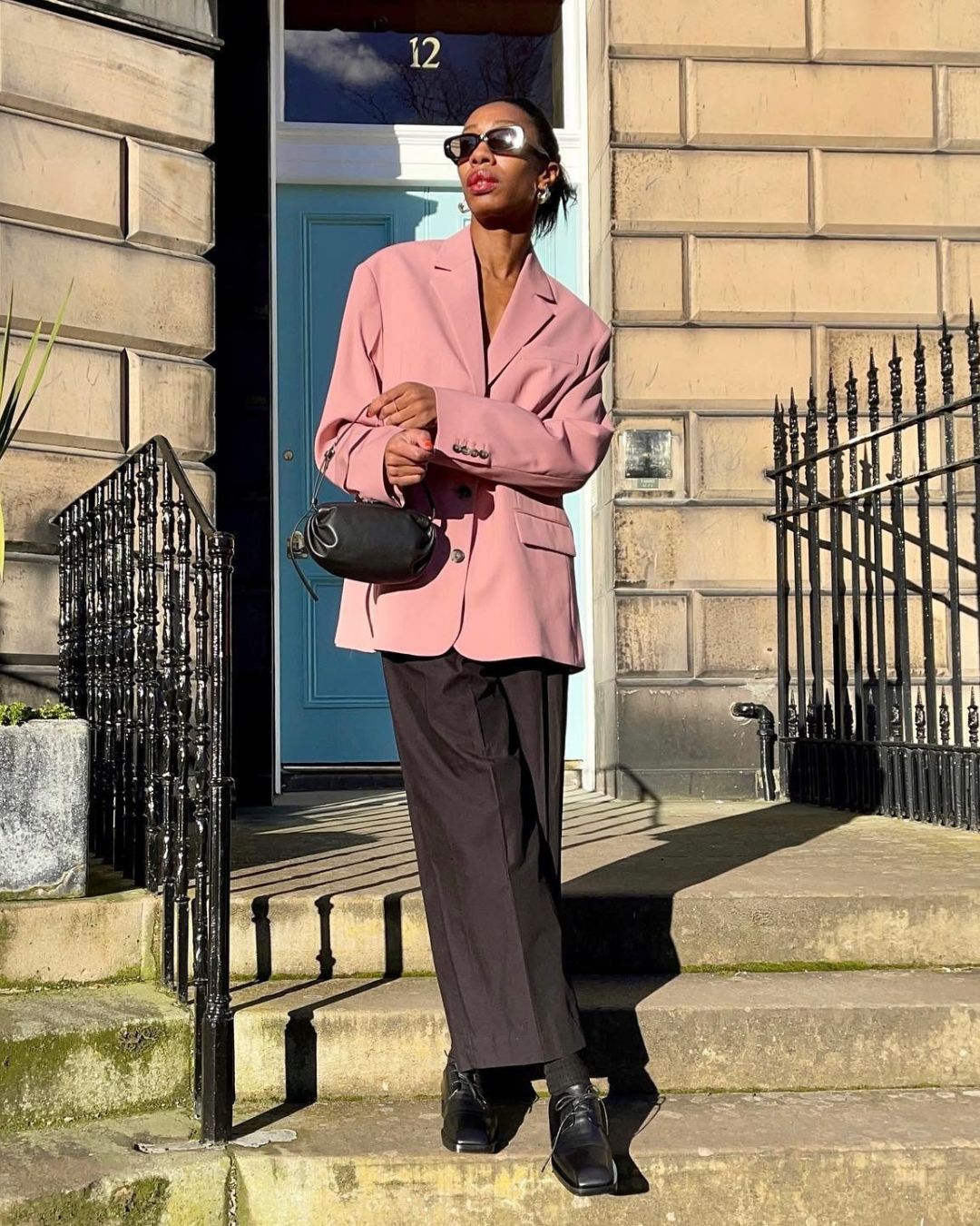Influencer @louisahatt stands outside wearing Oxford shoes, brown trousers and a pink blazer.