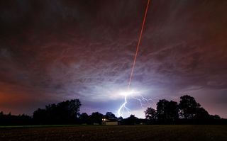A powerful laser beam shoots out of the Allgäu Public Observatory in southwestern Bavaria, Germany, on August 18, 2011, while lightning also flashes in the background.