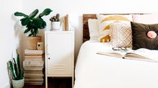 Locker bedside table in white, besides boho styled bed, with book pile stack and potted cacti and houseplant.