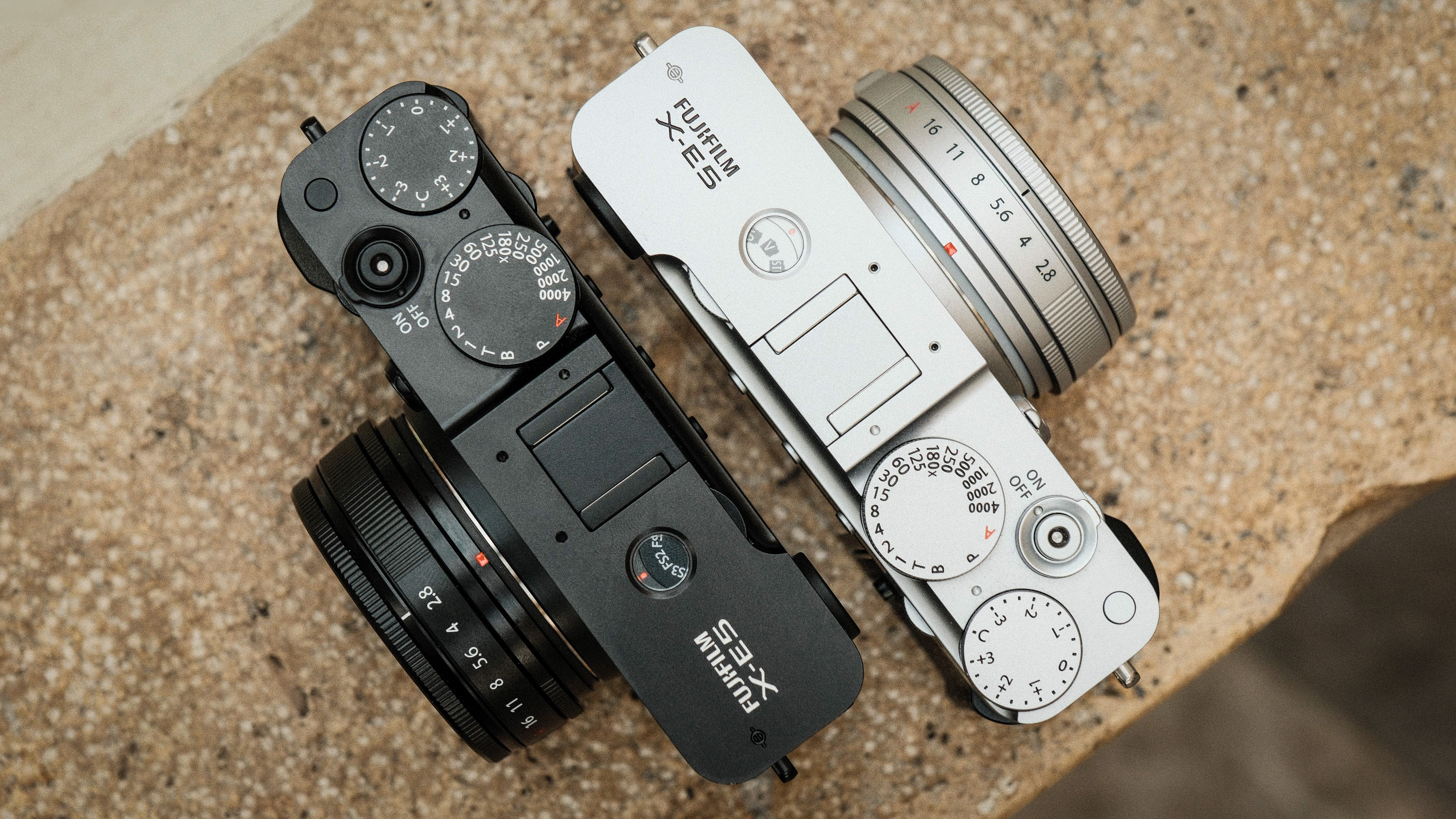 Two Fujifilm X-E5 cameras in black and silver next to one another on a stone wall