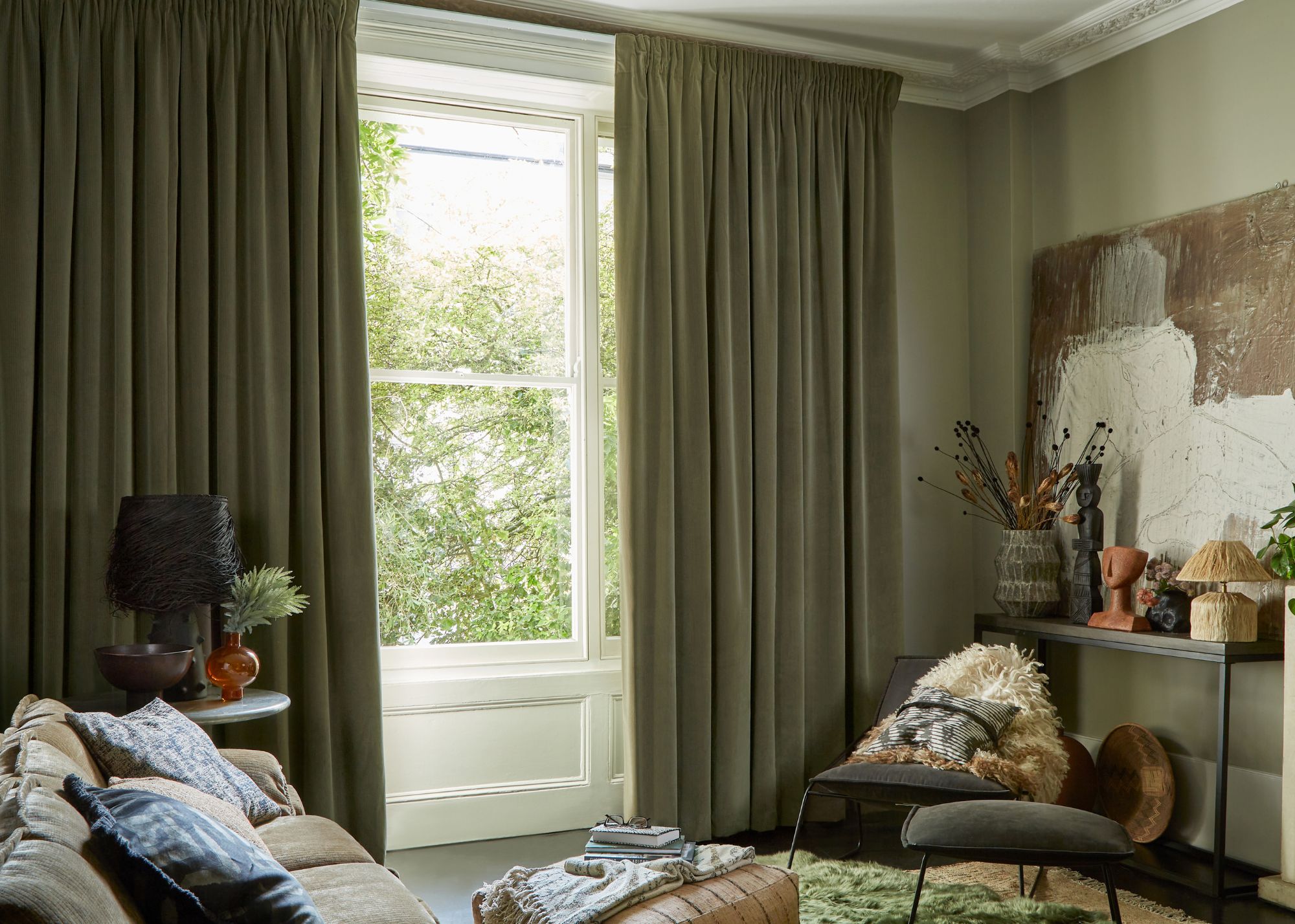A cozy living room with dark green pencil pleat curtains and light green walls.