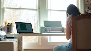 How to use a Cricut; a woman sits at a desk using a craft machine with a laptop