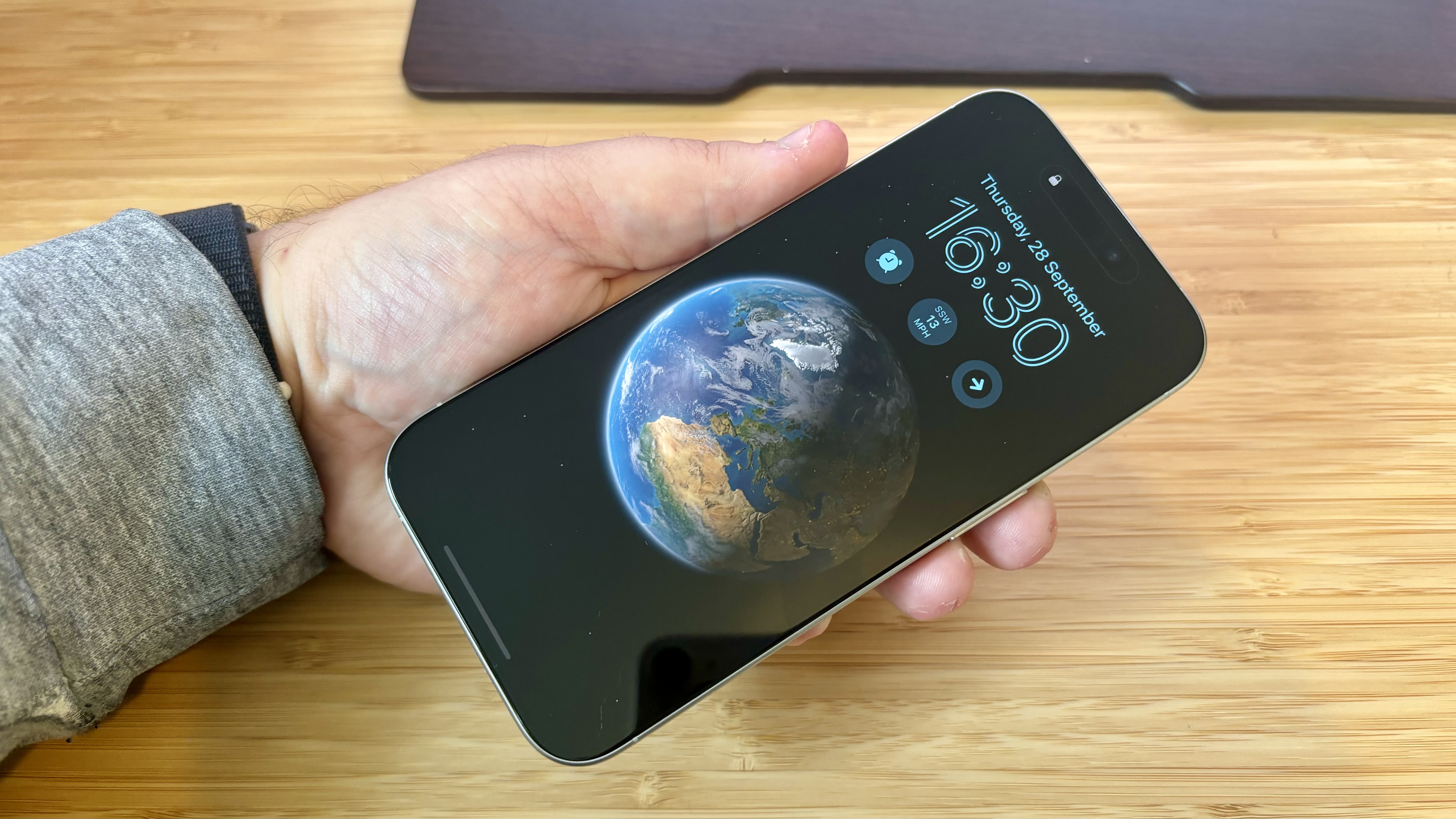 A grey titanium iPhone 15 Pro camera phone on a wooden desk