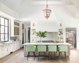 white kitchen with vaulted ceiling, island, orange lantern, blue range and green bar stools