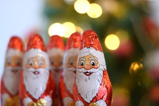 Several chocolate Santa's lined up in front of Christmas lights.