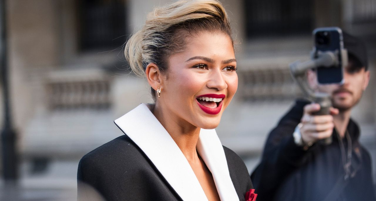 Zendaya greeting fans in Paris wearing a slicked back bun with red lipstick 