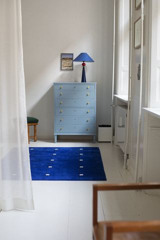 A corridor with a blue rug, light blue chest of drawers with a blue table lamp on top