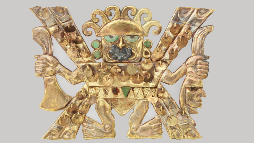 a gold figurine holds an axe in one hand and a severed human head in the other; he is accessorized with small bits of turquoise