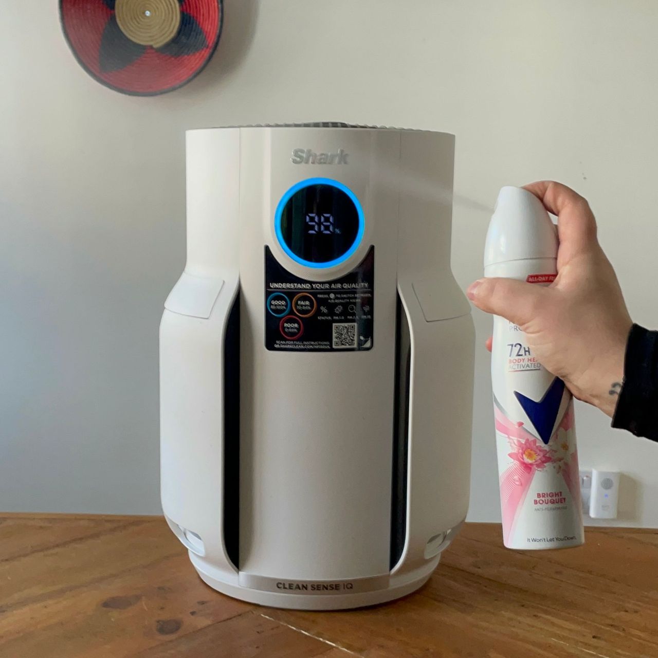 Shark NeverChange 5 Air Purifier sitting on a wooden table, with a deodorant can being sprayed towards it
