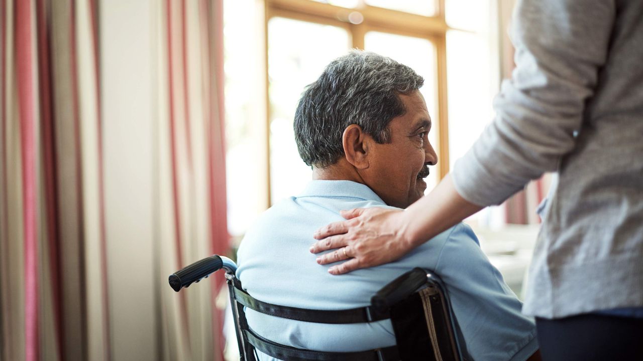 A man in a wheelchair gets a pat on the back from a caregiver.