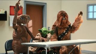 Scene from the animated/stop-motion T.V. show Robot Chicken (a show that parodies anything sci-fi). Here we see E.T. (small brown alien), Yoda (an even smaller green alien wearing a robe), and Chewbacca (a large furry humanoid wearing a bandolier). The 3 of them are sitting at a desk in a classroom, each with one arm raised ready to answer a question.