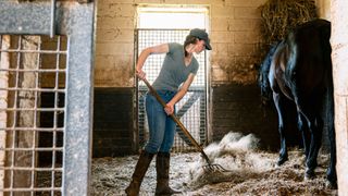 woman putting clean bedding in horse's stable