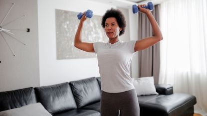 A woman performing a dumbbell shoulder press as part of a home workout