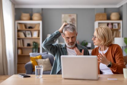 An older couple have an emotional discussion while looking at their laptop on the kitchen table.