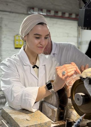 A women uses the cutting wheel on a glass to create a shape.