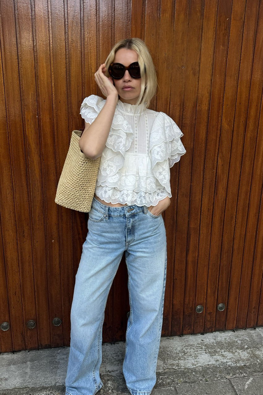 a woman wearing a lace white top, blue jeans, and a straw woven bag