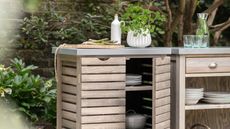 An outdoor cooking area with two freestanding spruce units with shelves and drawers, and metal worktops.
