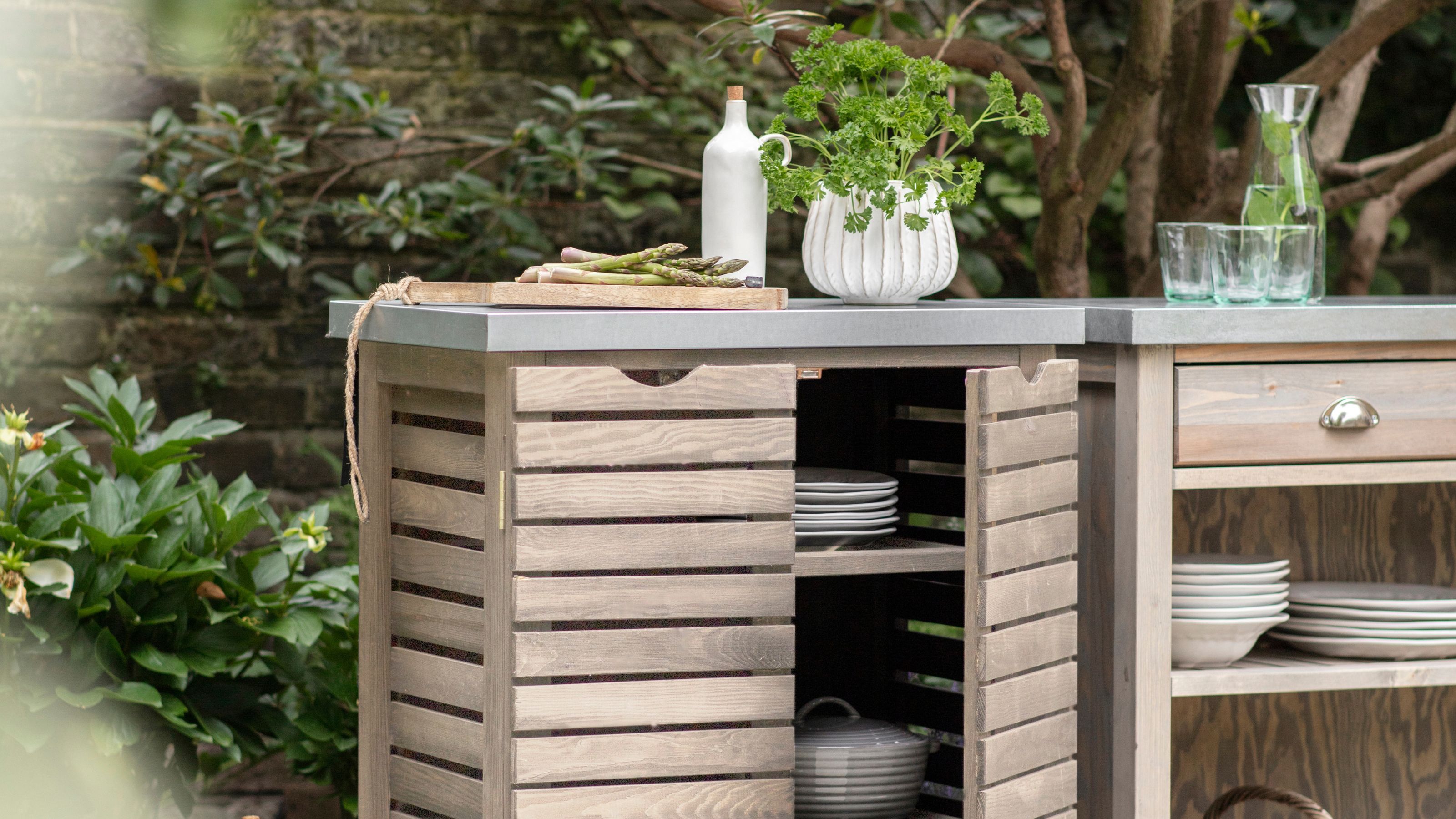 An outdoor cooking area with two freestanding spruce units with shelves and drawers, and metal worktops. 