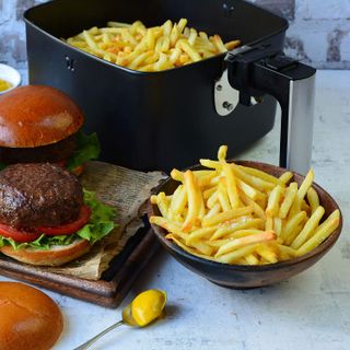 A black Breville air fryer filled with cooked French fries with burger in foreground