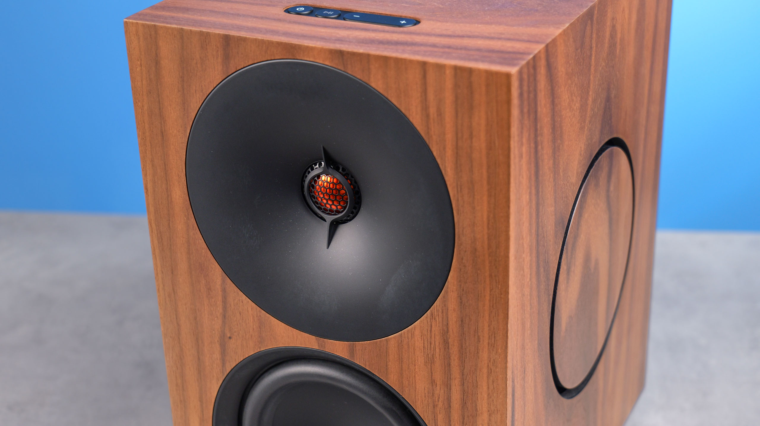 The Cambridge Audio L/R X tweeter, positioned on a stone surface with a blue background