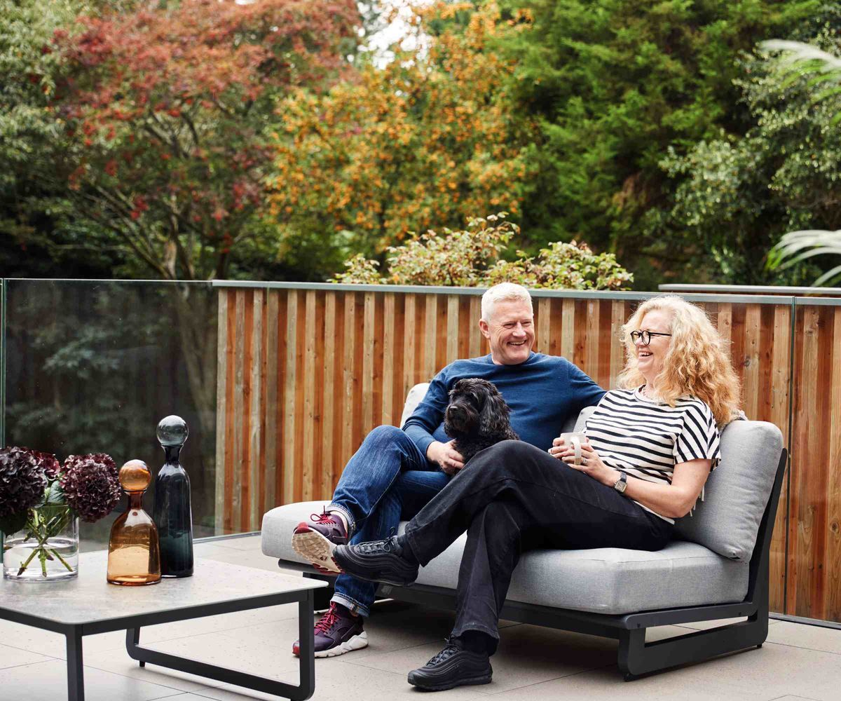Homeowners and their dog sitting on the balcony of their modern self build, built by Baufritz