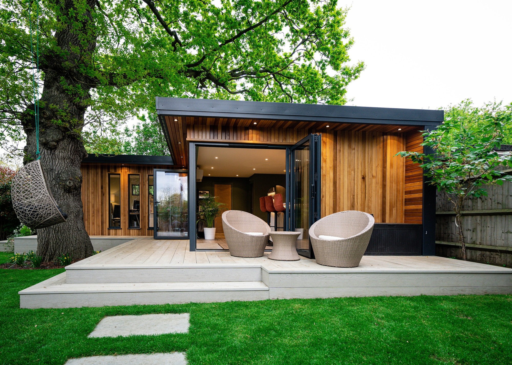 an L-shaped timber clad garden room with two tub chairs outside