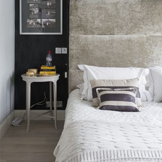 Room with black wall, with beige headboard and white and grey linen and a side table