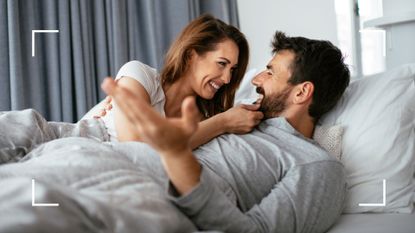 Man and woman laughing together in bed to demonstrate the yab yum sex position