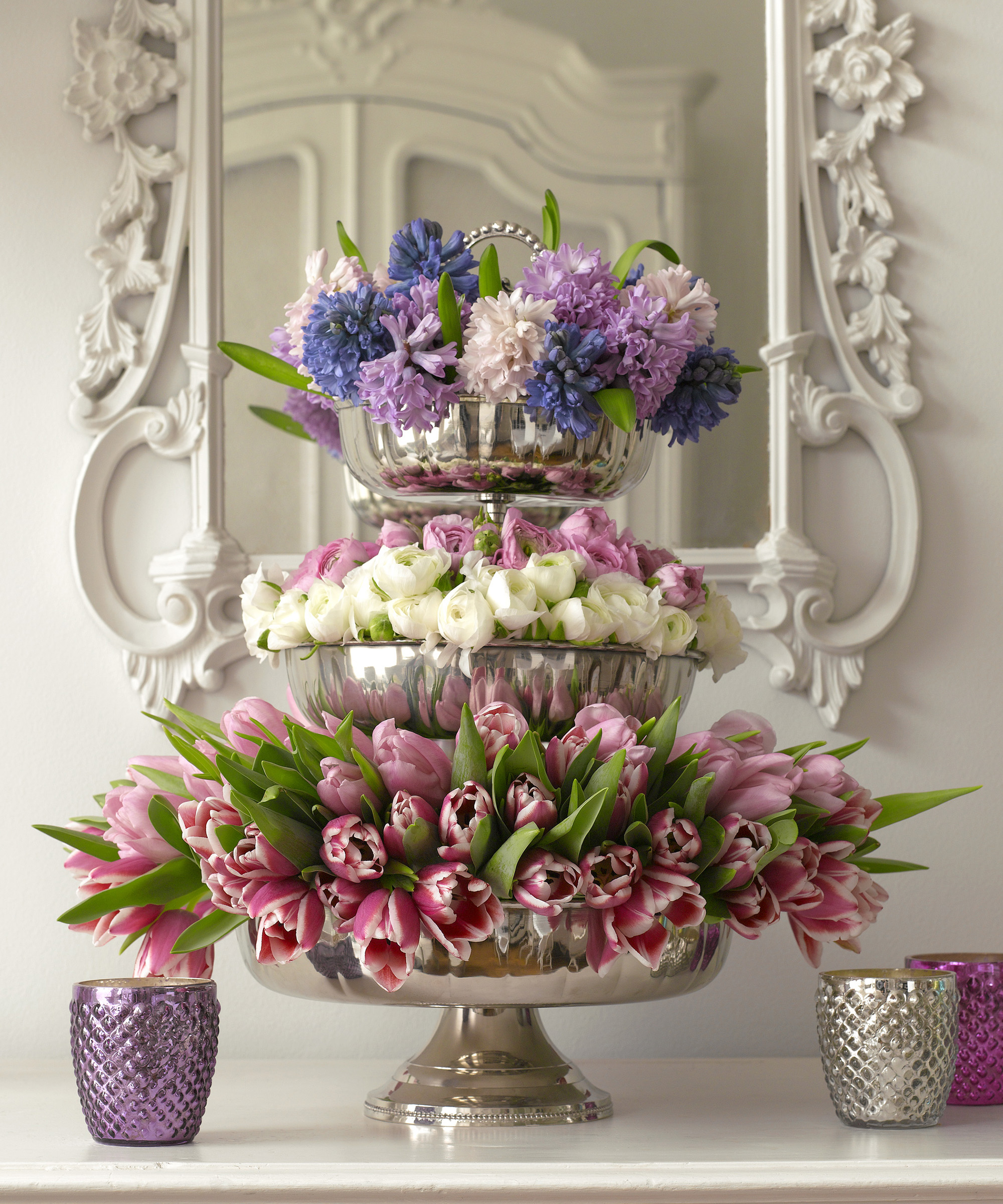 Three-tier silver cake stand filled with tulips, ranunculus, and hyacinths