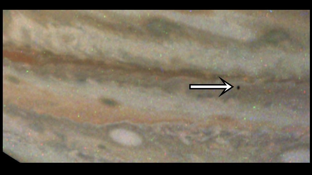 the close-up of a gas giant is striped with tans, browns, and some faint orange. A white arrow points to a small dark dot, the shadow of a moon.