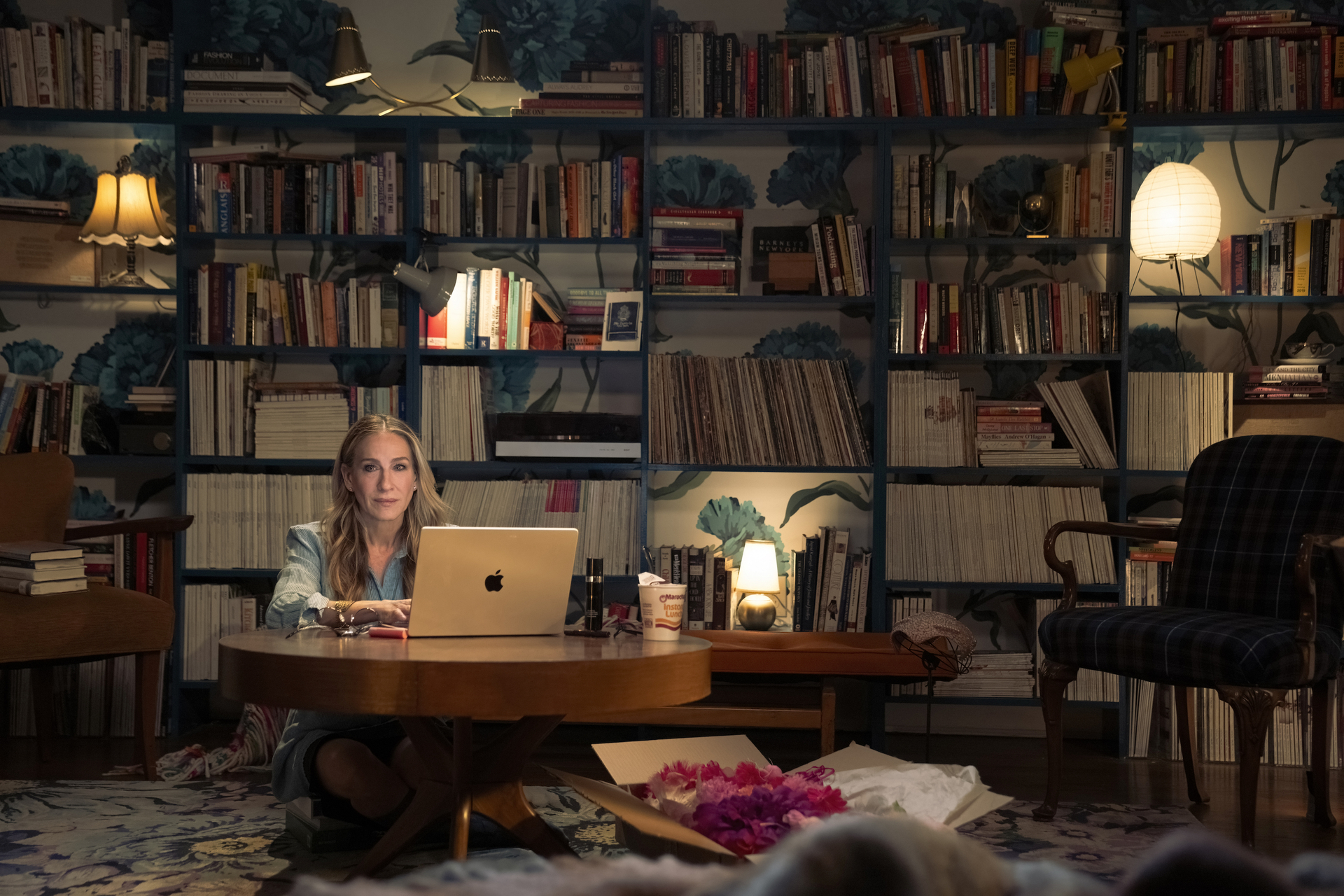 carrie bradshaw sits at her laptop on the floor in front of a wall of books