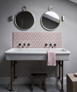 A double vanity unit with a pink and white tiled backsplash and two round mirrors